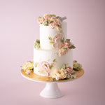 A two tier cake with a white buttercream base. The cake has both hand piped buttercream flowers and palette knife buttercream flowers. The flowers are in shades if ivory and pastel pink, and look incredibly realistic.