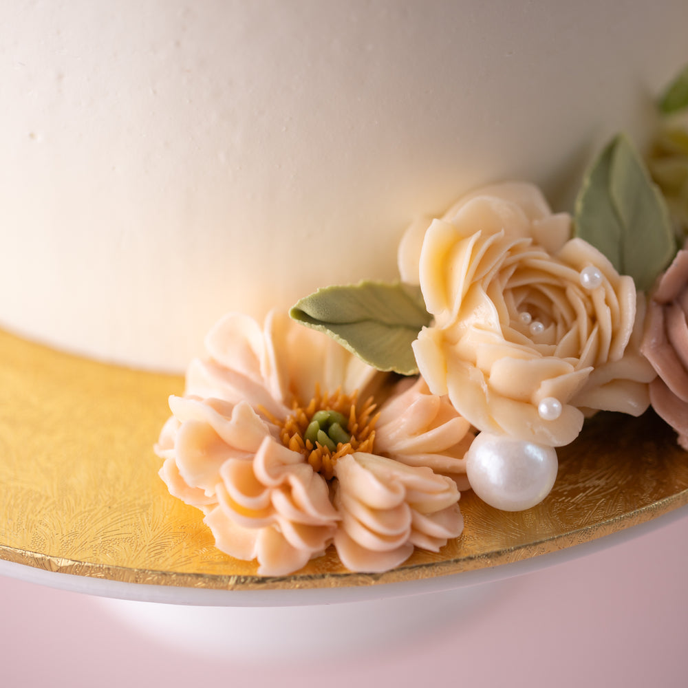 
                  
                    Load image into Gallery viewer, A close up on some of the hand piped buttercream flowers on the base of the cake and cake board. The flowers featured are ivory and peach in colour. There are also numerous edible sugar pearls in different sizes scattered around the flowers.
                  
                