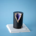 A tall and slim cake, this cake is covered in a dark bluish purple fondant. The fondant has speckles of gold splattered on it that resemble stars. A chunk of the cake has been cut out adn replaced with edible purple rock candy that resemble Amethyst gems, so the cake looks like a geode.