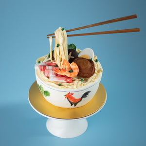 
                  
                    Load image into Gallery viewer, A cake that has been decorated to look like a bowl of noodles. There are fondant shrimp, sliced meat, abalone and spring onions on top of the noodles. Floating above in the :anti gravity&amp;quot; style is a pair of chopsticks also made of fondant, holding into the fondant noodles.
                  
                