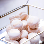 A transparent box filled with small, light pink macarons. The macarons have a streak of gold painted on them for a classy, elegant effect.