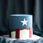 A cake heavily inspired by Captain America. It has a dark blue buttercream base, and wears Captain America's uniform, along with a white star in the middle. The cake is elegant and sophisticated.