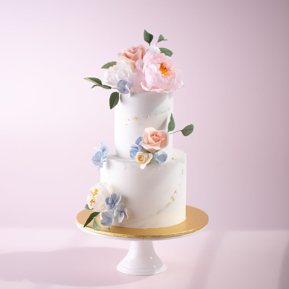 A two tier cake with a white and grey marbled buttercream base. The cake has many handcrafted sugar flowers on the top, middle and bottom, in various breeds and colours. The flowers look incredibly realistic.