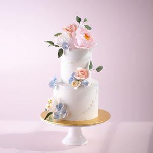 
                  
                    Load image into Gallery viewer, A two tier cake with a white and grey marbled buttercream base. The cake has many handcrafted sugar flowers on the top, middle and bottom, in various breeds and colours. The flowers look incredibly realistic.
                  
                