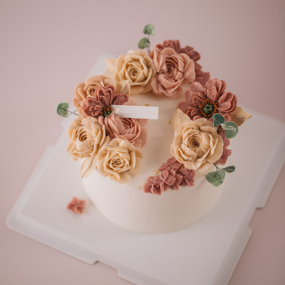 Ivory buttercream base with various shade of pink buttercream flowers on top in a crescent shape.