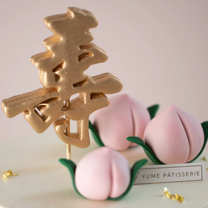 
                  
                    Load image into Gallery viewer, Three little hand crafted fondant peaches that are pink in colour with vibrant green leaves. Next to them, there is a gold fondant &amp;quot;shou&amp;quot;.
                  
                