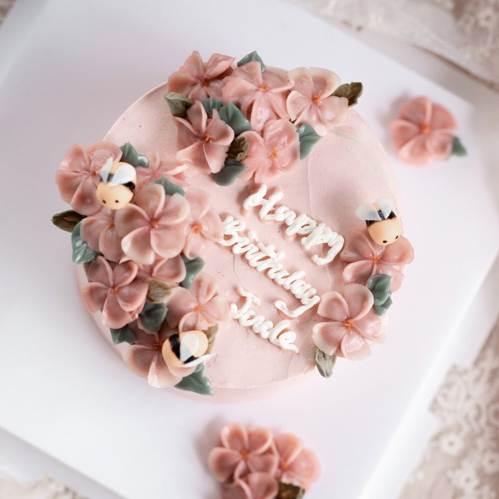 
                  
                    Load image into Gallery viewer, A light pink buttercream cake with pink buttercream flowers on top, decorated with little fondant bees. &amp;quot;Happy Birthday&amp;quot; is written in buttercream cursive in the middle of the cake.
                  
                