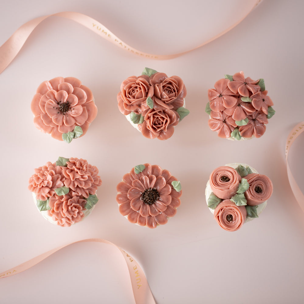 6 cupcakes with assorted pink hand piped buttercream flowers on them.  The flowers look incredibly realistic.