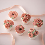 6 cupcakes with assorted pink hand piped buttercream flowers on them. The flowers look incredibly realistic.