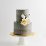 A two tier wedding cake with a concrete grey buttercream base. The buttercream has streaks of lighter grey marbled into it. There are some light pink and ivory edible sugar roses in the middle, along with some pale edible green sugar leaves. The flowers look incredibly realistic.