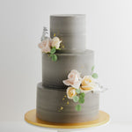 A three tier wedding cake with a concrete grey buttercream base. The buttercream has streaks of lighter grey marbled into it. There are some light pink and ivory edible sugar roses in the middle, along with some pale edible green sugar leaves. The flowers look incredibly realistic.