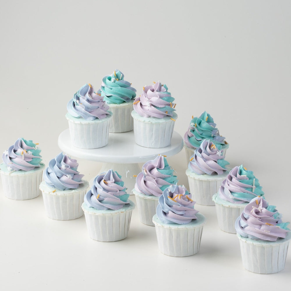Multiple cupcakes with tall swirls of blue and purple ombre buttercream. The cupcakes have orange sprinkles on them for slight contrast.