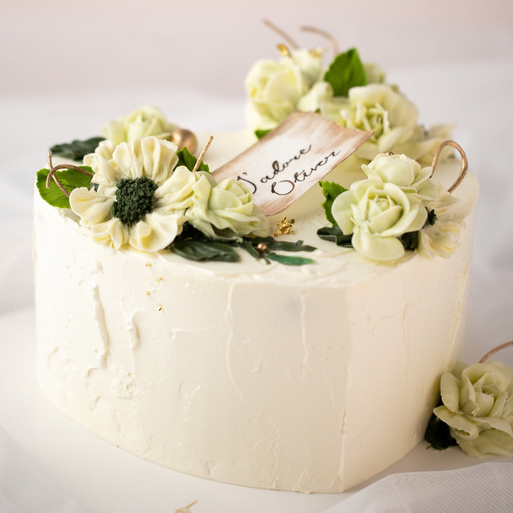 
                  
                    Load image into Gallery viewer, A heart shaped cake with white buttercream base, and light green and ivory buttercream flowers on top. Gold pearls and gold leaves are scattered around the cake delicately. There is a wafer paper note in the middle of the heart that says &amp;quot;J&amp;#39;adore Oliver&amp;quot;.
                  
                