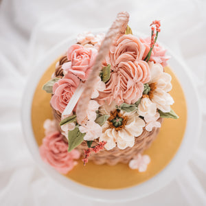 
                  
                    Load image into Gallery viewer, A cake that has been decorated to look like a flower basket. The outside has light brown buttercream that has been piped to resemble a woven basket, and it has assorted buttercream flowers in pink, ivory and white spilling out of it. It is a realistic flower basket cake.
                  
                