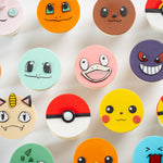 Cupcakes that have round fondant toppers that look like different pokemon. Three of them are types of Pokeballs. The pomemon faces are all extremely cute and true to the anime.