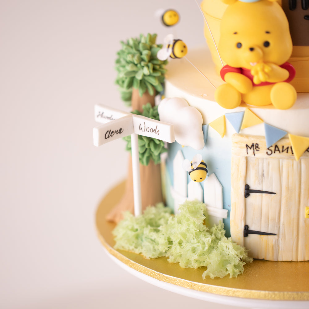 
                  
                    Load image into Gallery viewer, A fondant street sign that says &amp;quot;Hundred Acre Woods&amp;quot;. There is a white fondant picket fence in the back, and also some green sponge cake that resembles bushes.
                  
                
