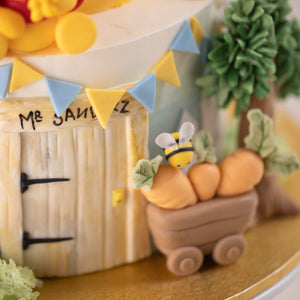 
                  
                    Load image into Gallery viewer, A fondant cart carrying some fondant carrots, with a little fondant bee peering at it. Next to the cart is a fondant door with hand painted details. The door resembles the door in Winnie the Pooh books.
                  
                