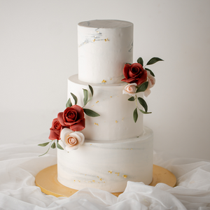 
                  
                    Load image into Gallery viewer, A tall three tier minimalistic wedding cake, with a white and light grey marble buttercream base. The cake has some bright red and light pink edible sugar roses, along with some darker green edible sugar leaves. The white and grey marbled buttercream has some edible gold leaf carefully placed, to give it a stunning contrast.
                  
                