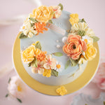 A pale blue cake with bright coral and yellow hand piped buttercream flowers. The cake also has some sugar pearls delicately scattered on top. The flowers look incredibly lifelike.