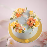 A pale blue cake with bright coral and yellow hand piped buttercream flowers. The cake also has some sugar pearls delicately scattered on top. The flowers look incredibly lifelike.