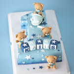 A large cake carved into the number "one" with an ombre blue buttercream base. There are four fondant bears on the cake, one of which is driving a light blue car. There are white and blue fondant stars in various shapes all around the cake. At the base of the "one", there are 3D fondant alphabet blocks that spell the name "Kaius".