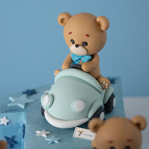 
                  
                    Load image into Gallery viewer, A close up on the fondant bear riding a car. The fondant bear has a blue bow and a concerned expression on its face. It is driving a light blue convertible.
                  
                