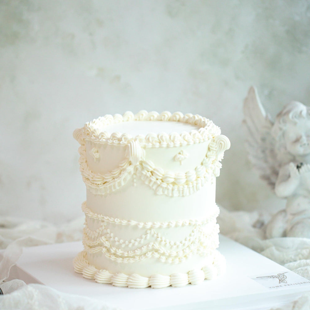 White Vintge Buttercream Birthday Cake Singapore. A white buttercream cake with baroque vintage hand piped designs on the cake that resemble frills.