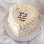 A beautiful white buttercream heart shaped cake with vintage baroque styled buttercream piping. The buttercream is white, giving the cake an elegant, princess-y feel. The cake is extremely beautiful.