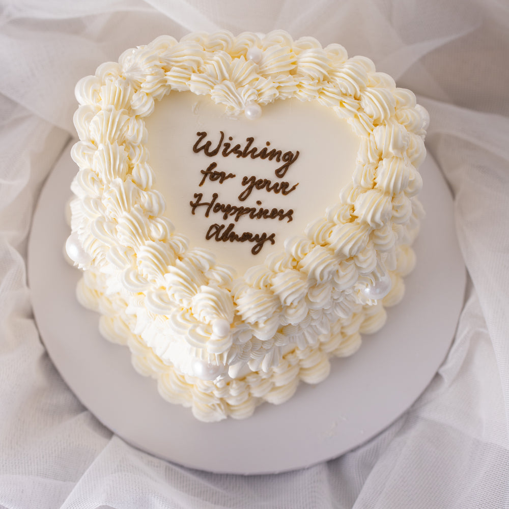 A beautiful white buttercream heart shaped cake with vintage baroque styled buttercream piping. The buttercream is white, giving the cake an elegant, princess-y feel. The cake is extremely beautiful.