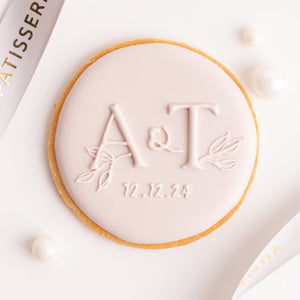 
                  
                    Load image into Gallery viewer, A round cookie with the initials &amp;quot;A&amp;amp;T&amp;quot; on it in cursive. Below the initials is the date &amp;quot;12.12.24&amp;quot;. The cookie is decorated with royal icing in a soft, pastel pink.
                  
                