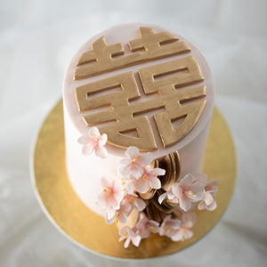 
                  
                    Load image into Gallery viewer, A close up on the &amp;quot;Xi&amp;quot; fondant cake topper. It is pained gold, and has a round shape. The pale gold pairs with the light pink cake beautifully.
                  
                