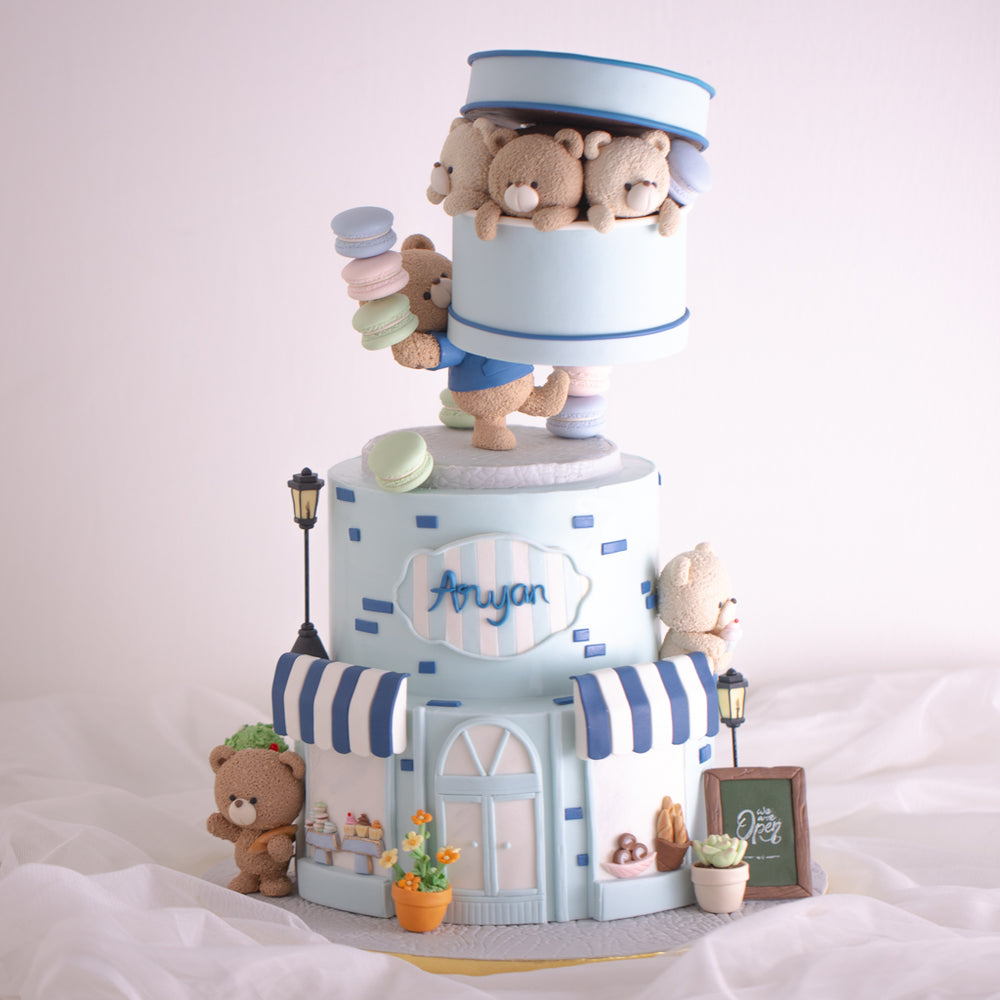 A three tier blue and white Parisian Cafe themed birthday cake with fondant teddy bears. There are many small fondant details on the cake bringing it to life.